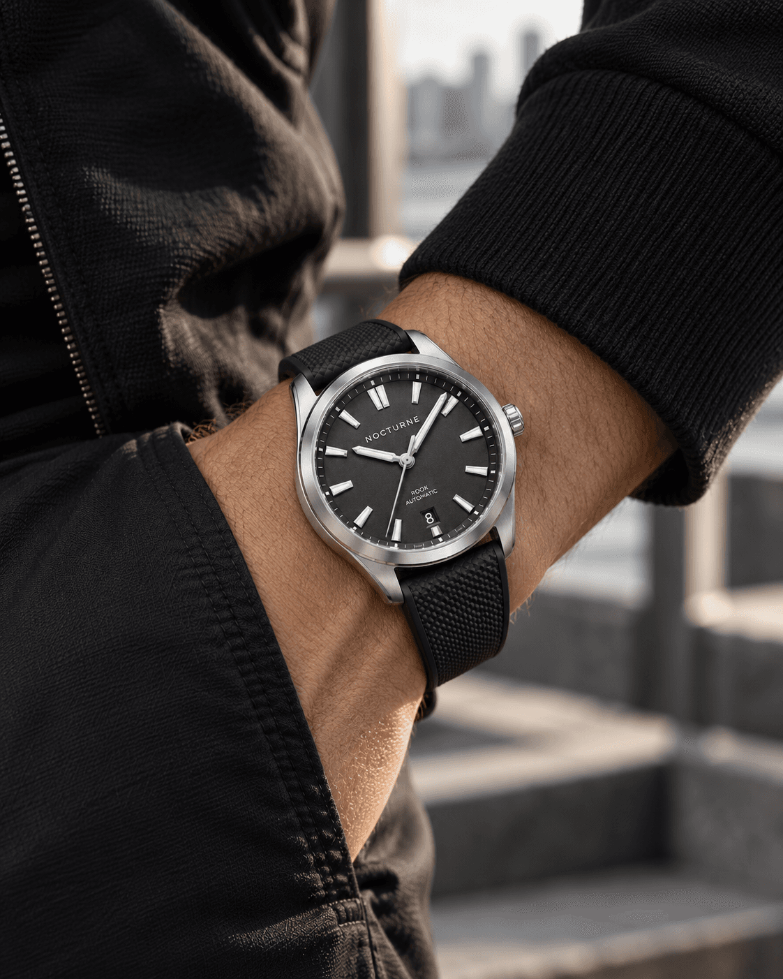 Rook Automatic on the wrist with a dark jacket in an urban setting