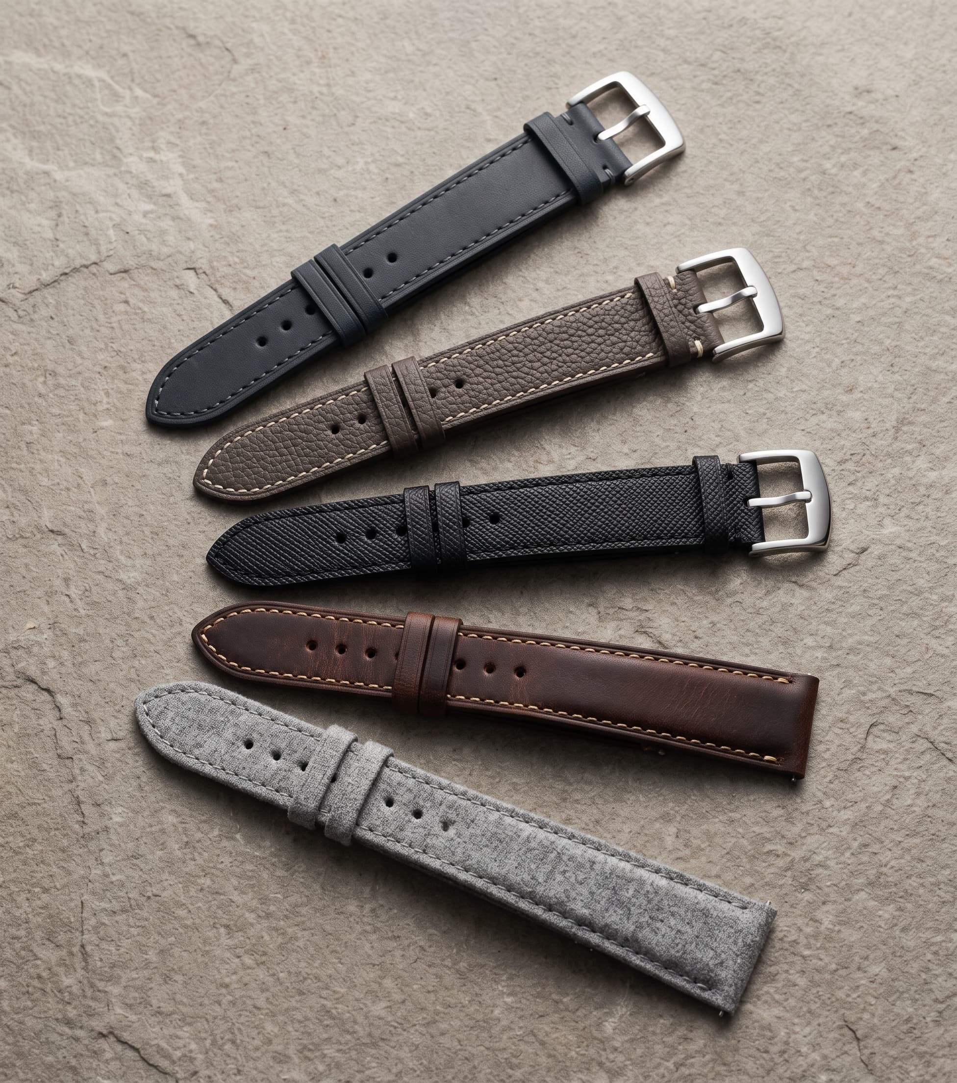 Five NOCTURNE leather and technical straps arranged on a warm stone surface
